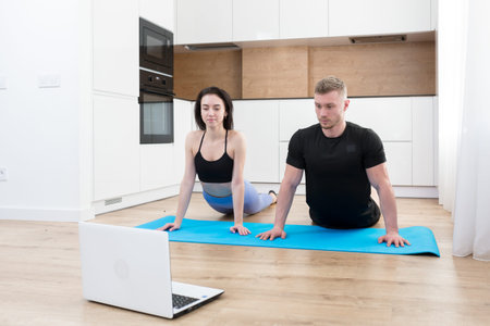Young couple man and woman doing fitness at home online using laptop, doing online with trainer on...