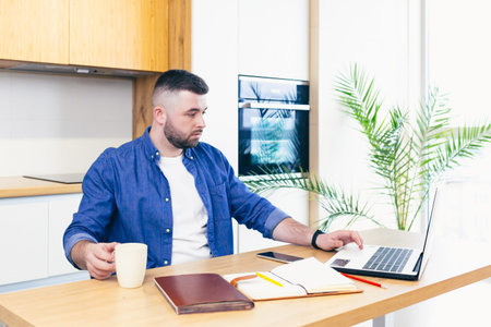 man doing business while staying at home. sitting in the kitchen at the table and using a laptop