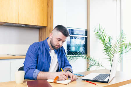 man doing business while staying at home. sitting in the kitchen at the table and using a laptopの写真素材