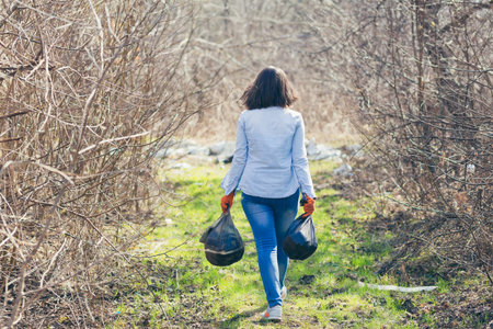 Young beautiful female volunteer collects plastic garbage in the forest and park, volunteer holding...
