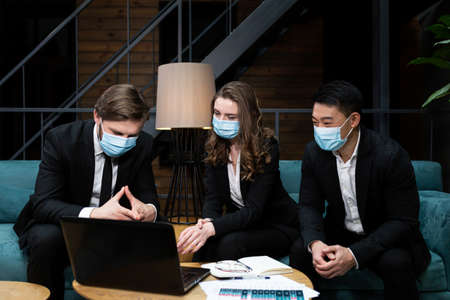 Group of men and woman hold business meeting, near laptop, wearing protective medical masks on face, in conference room, business meetingの写真素材