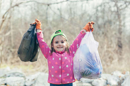 The little girl collected two bags of garbage and plastic bottles in the forest and the park, the girl is happy that she helped the volunteers to clean the parkの写真素材