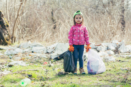 The little girl collected two bags of garbage and plastic bottles in the forest and the park, the girl is happy that she helped the volunteers to clean the parkの写真素材