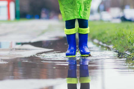 Close-up photo of a little girl jumping in boots on puddles, blue bootsの写真素材