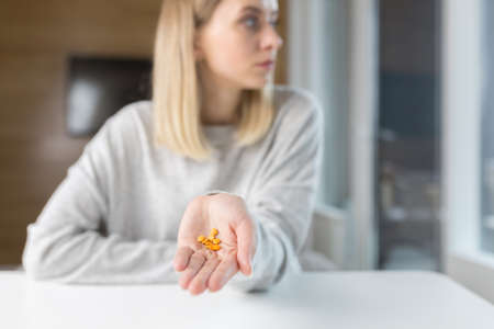 Close-up shot of a woman's hand holding a few yellow pillsの写真素材