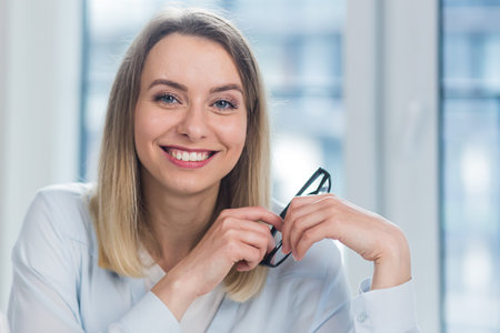 Close-up portrait a caucasian young blonde woman indoors looking at camera and smiling. Cute Happy...