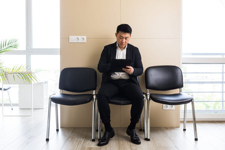 Asian businessman man, in the waiting room sitting on a chair near the reception of the office...