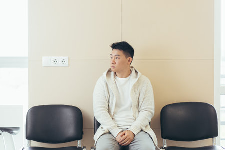 young asian man waiting for an interview or meeting sitting in the hallway in the waiting room. Student or entrant in the reception for exam or employment hr. Male patient in office a hospital clinicの写真素材