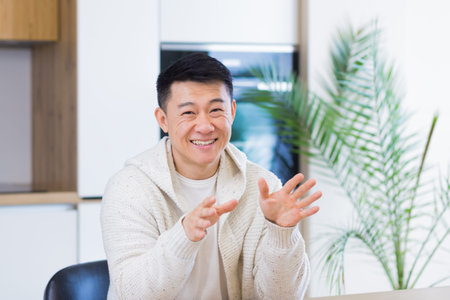 Asian man talking online on video call at home room with headset. Male in casual clothes looking at...