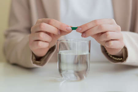 the woman's hands open the tablet in half, and dilute the medicine with a glass of waterの写真素材