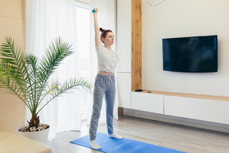 Young beautiful woman performing morning workout and fitness exercises at home