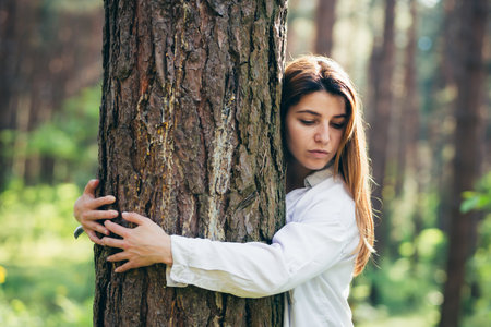 Young beautiful female volunteer hugs a tree with love in the forestの写真素材