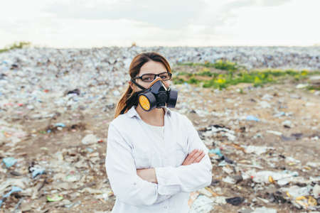 Female scientist in a protective respirator mask at a landfill assesses the level of environmental pollutionの写真素材