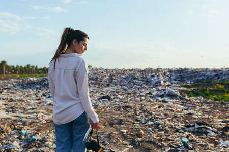 view of a woman from the back on the background of the landfill holding a respiratorの写真素材