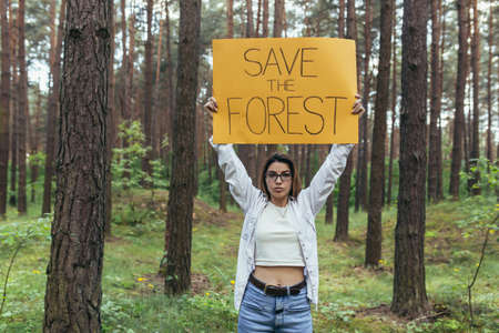 young woman volunteer in the woods pickets and holds a poster save the forestの写真素材