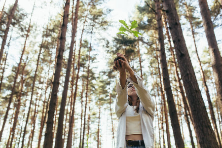Young female volunteer plants a forest, holding an oak tree seedling in her hands