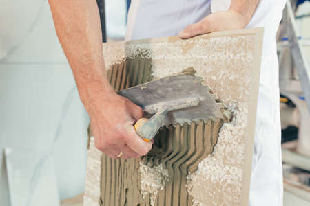 Male worker professional mounts ceramic tile in bathroom photo with close spatula with glueの写真素材