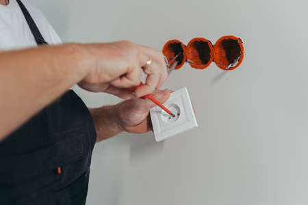 Male worker professional electrician mounts an electrical outlet in the apartment after repair, close-up photo of the installerの写真素材