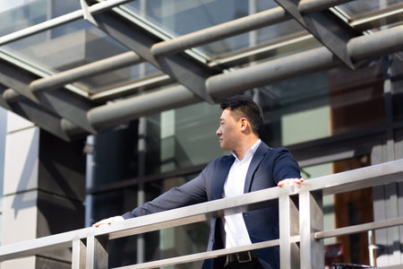 Asian businessman boss stands near his office center on the balcony in a dark color business suit