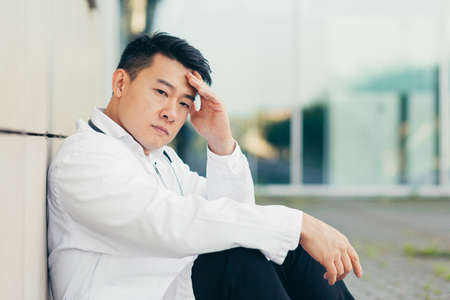 portrait Doctor Asian man tired after work sitting on the floor near the clinic disappointed with the resultの写真素材