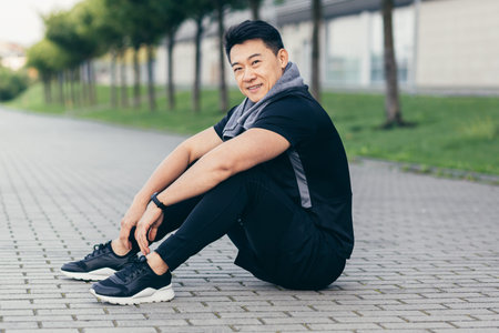 asian man after fitness workout and jogging sitting on the ground tired resting