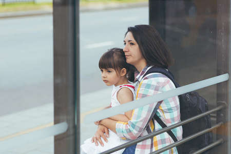 A young woman with her daughter is waiting for a public bus at the bus stationの写真素材