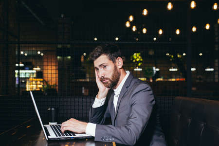 Successful businessman working on laptop during lunch break sitting in hotel restaurant, tired doing taskの写真素材