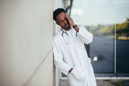 male doctor at the clinic holding his head has health problems and tired after a hard day, depressed did not get the desired result, afro american doctor is sadの写真素材