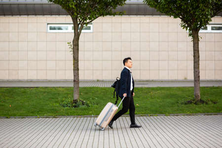 Successful asian businessman near airport and bus station goes with suitcases serious tourist looking at cameraの写真素材