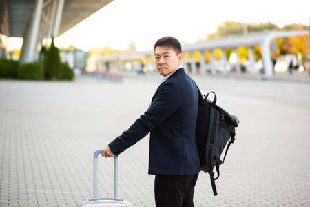 Successful asian businessman near airport and bus station goes with suitcases serious tourist looking at cameraの写真素材