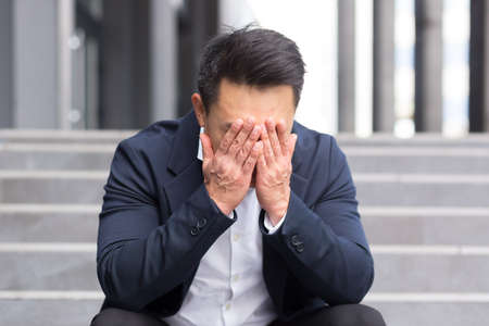 Asian businessman has a severe headache sitting on the stairs near the officeの写真素材