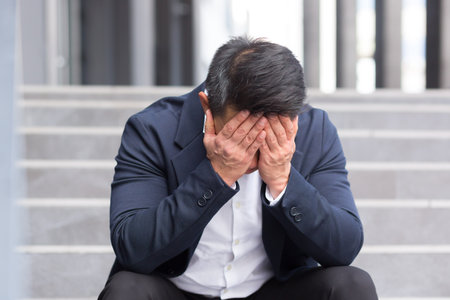 Asian businessman has a severe headache sitting on the stairs near the officeの写真素材