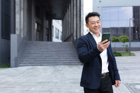 Portrait of Asian cheerful and successful businessman near office in business suit got good news read good news onlineの写真素材