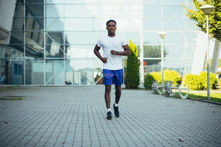 man on morning run, young african american athlete running near stadiumの写真素材