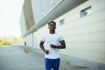 man on morning run, young african american athlete running near stadiumの写真素材