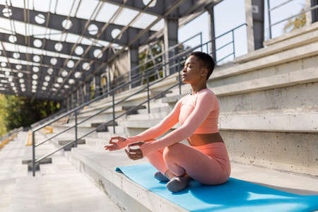Young beautiful woman in a pink tracksuit meditating in the stadium in the morning, fitness trainer resting after trainingの写真素材