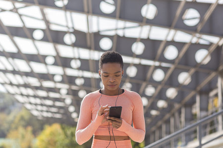 African American woman walks in the morning near the stadium before jogging listens to motivational...
