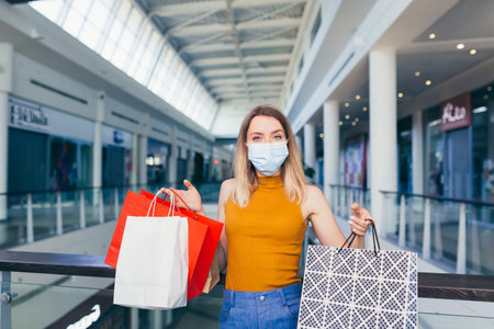 Female shopper in a protective medical mask shopping in supermarkets holding gift bags