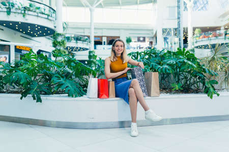 young happy after shopping woman talking on cell in mall. Satisfied joyful female shopaholic with gift colored paper bags in hands. Mobile phone conversation. Smiling joy Stand ang sincerely tellsの写真素材