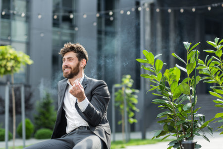 Caucasian bearded business man smoking cannabis outdoors sitting on city park bench on urban street...