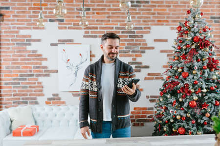 A serious and focused man is corresponding on a mobile phone near the Christmas tree at homeの写真素材