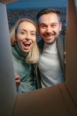 Young beautiful happy couple joyfully open packages of boxes with gifts for New Year and Christmas...
