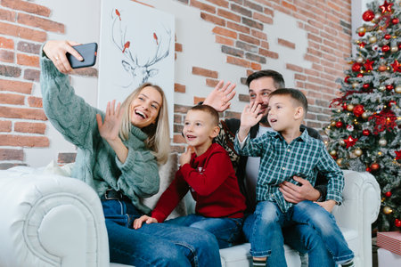 Beautiful happy married couple with two children using smart phone talking to friends or family congratulates Merry Christmas by video call conference app. Modern technology New Year 2022 congrats.の写真素材