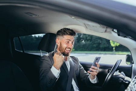 Excited emotional adult businessman driving car rejoicing online victory achievement lottery...