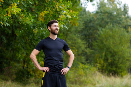 Close up portrait young happy bearded man standing in nature between forest trees relaxes, breathes...