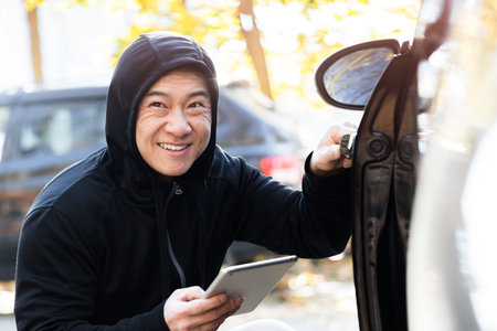 male bandit thief car thief asian uses a tablet to turn off the car alarm