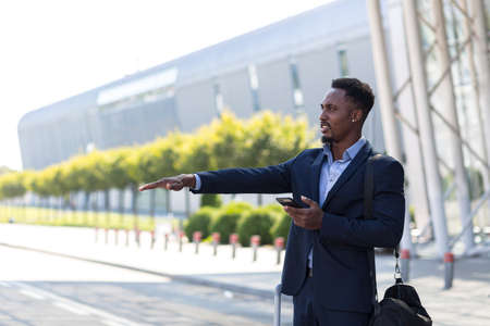 Male businessman near airport with suitcase, african american trying to catch taxi carの写真素材