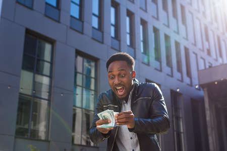 Happy successful African American guy counts, waves, throws, show off, flaunt, cash money background urban city street building. Man looking at camera Celebrate Winner success in betting stock marketの写真素材