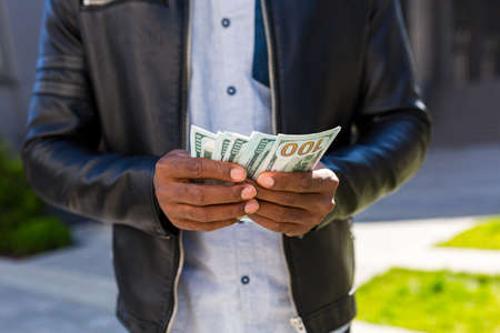Close-up photo of the hand of an African American businessman counting cash dollarsの写真素材