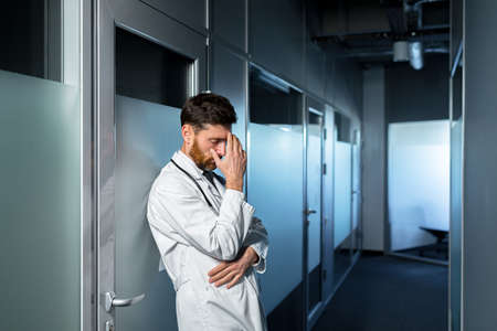 Tired doctor overworked at work, has a severe headache, feels bad, a man in the corridor of the clinic is disappointed with the resultの写真素材